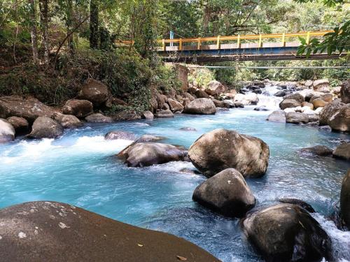 a river with rocks and a bridge with a train at Cabaña bosque río celeste in San Rafael