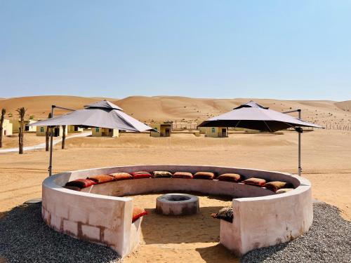 a fire pit in the middle of a desert with umbrellas at Al Salam Desert Camp Bidiya in Bidiyah