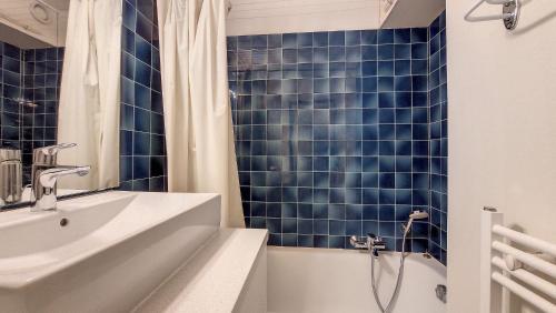 La salle de bains est pourvue de murs carrelés bleus, d'un lavabo et d'une baignoire. dans l'établissement Relais S9, à Saint-Jean-dʼAulps