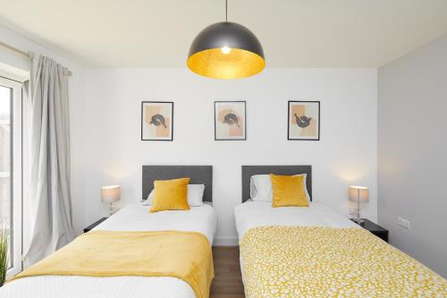 two beds in a room with white walls and yellow pillows at Derby Train Station Roof Terrace House in Derby