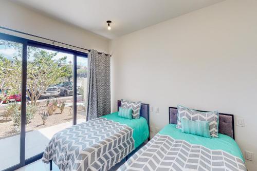 two beds in a room with a large window at Tramonti Condo Tari #107 in Cabo San Lucas