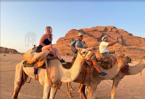 three people riding on the backs of camels in the desert at Lma Luxury Camp in Wadi Rum