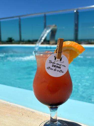 a drink with an orange slice in front of a swimming pool at Hotel Amaromar in Pontal do Paraná