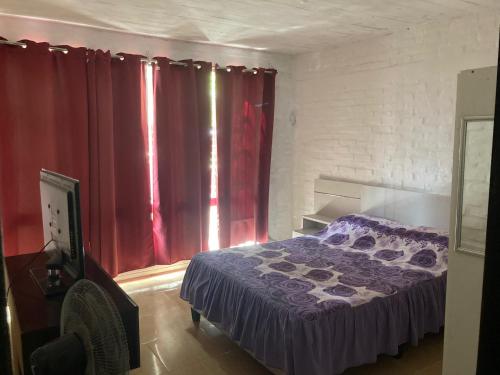 sypialnia z fioletowym łóżkiem i czerwonymi zasłonami w obiekcie Casa en San Luis w mieście La Floresta