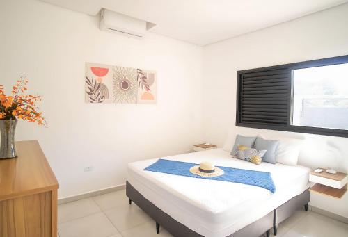 a white bedroom with a bed with a hat on it at Paraíso Pé na Areia em Boracéia - Desfrute da conveniência de ter a praia no seu quintal in São Sebastião