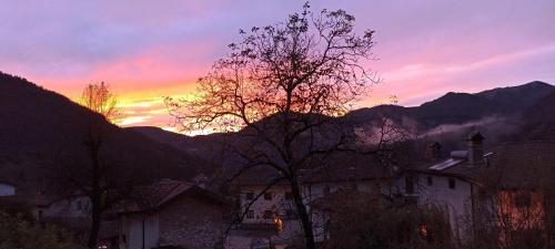 a sunset in the mountains with a tree and buildings at Cjase di Doro in Illegio