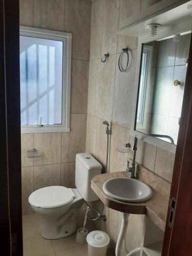 uma casa de banho com um WC, um lavatório e uma janela em Condomínio Cordeiro em Arroio do Sal