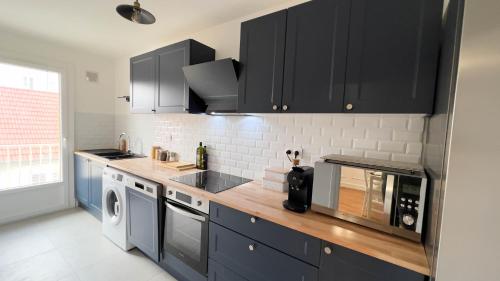 une cuisine avec des armoires noires et un lave-linge/sèche-linge dans l'établissement Appartement 4 étoiles en centre ville de Vichy - Le Basile, à Vichy