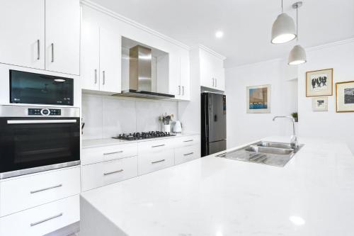 a white kitchen with white counter tops and appliances at Flagship Villa in Trinity Beach