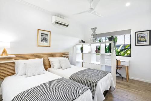 two beds in a room with white walls and a desk at Flagship Villa in Trinity Beach