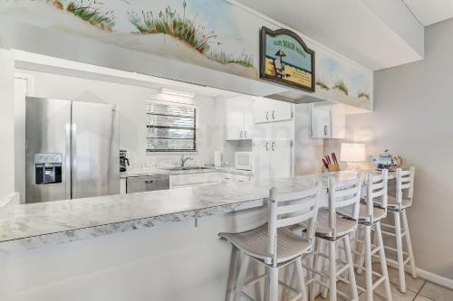 a white kitchen with a large counter with stools at Amelia By The Sea 110 in Fernandina Beach