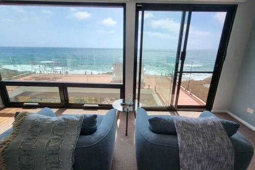 a living room with two blue chairs and a view of the ocean at Heathcliff. Stunning ocean views! in Boat Harbour