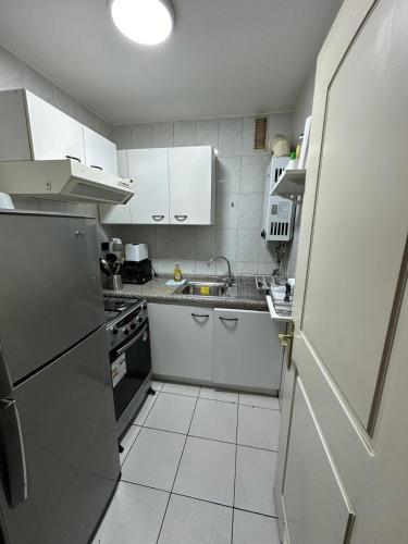a small kitchen with white cabinets and a refrigerator at Depto Las Condes- Est Español in Santiago