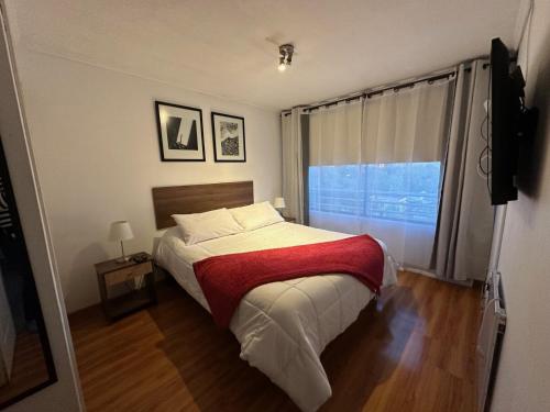 1 dormitorio con 1 cama con manta roja y ventana en Depto Las Condes- Est Español, en Santiago