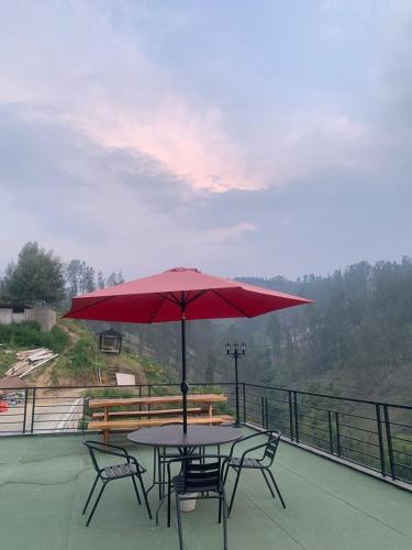a table and chairs with a red umbrella on a balcony at Hotel Nature Bromo and Resort in Pasuruan