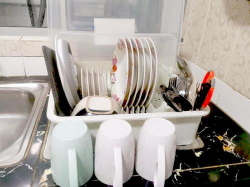 eine Küchentheke mit einem Geschirrregal mit Geschirr in einer Spüle in der Unterkunft Putatan Platinum Apartment with Pool in Kota Kinabalu