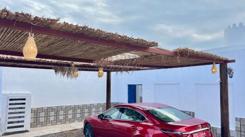 a red car parked under a straw roof at Wadi Shab Beach House in Ramlah