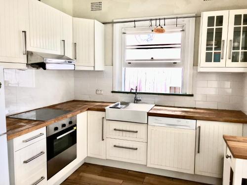 eine Küche mit weißen Schränken, einem Waschbecken und einem Fenster in der Unterkunft Study/Sun room attached MQ Park/Uni/Eastwood/Ryde Spacious room in Sydney