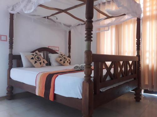 1 dormitorio con cama de madera con dosel y sábanas blancas en Sasagara Beach Villa, en Tangalle
