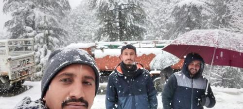 three men standing in the snow with an umbrella at Shimla Hills Apartments 2BHK in Shimla