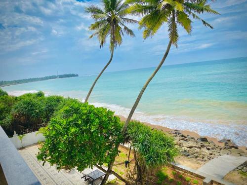 Blick auf einen Strand mit zwei Palmen und das Meer in der Unterkunft Sevenra Grand Beach Hotel in Ambalangoda
