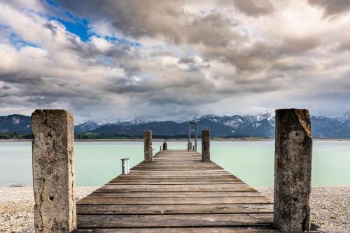 a wooden pier on a lake with mountains in the background at Seehotel und Appartements Schnöller in Rieden am Forggensee