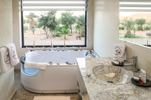 a bathroom with a tub and a large window at Yakout Merzouga Luxury Camp in Merzouga