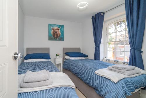 two beds in a bedroom with blue curtains and a window at The Old Mill Cottage in Fakenham