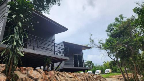 une maison noire avec un balcon et deux chaises dans l'établissement Riverhill khaoyai บ้านกล่อง, à Ban Bung Toei