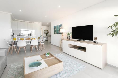 a white living room with a tv and a table at Zahra Place - Stylish Flat in Nazaré