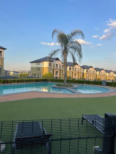 a building with a palm tree and a swimming pool at Apartment in Kikuyu, Waterfall in Midrand