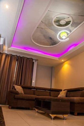 Résidence l'Appart في ياوندي: غرفة معيشة مع أريكة وسقف مع أضواء أرجوانية