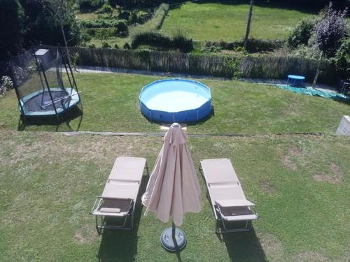 ein Sonnenschirm und zwei Liegestühle und ein Pool in der Unterkunft Casa moderna julio y agosto in Ferrol