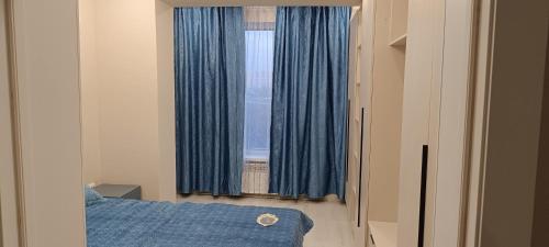 Schlafzimmer mit einem Bett und einem Fenster mit blauen Vorhängen in der Unterkunft Квартира in Almaty