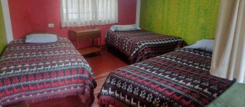 three beds in a room with red and green walls at Hospedaje La Ñusta in Ollantaytambo