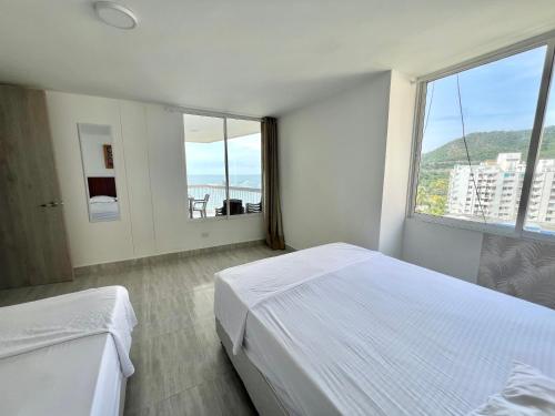 Habitación blanca con 2 camas y ventana grande. en Caribbean Venture Apto 901- Rodadero, Santa Marta, en Santa Marta