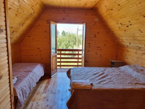 Habitación de madera con 2 camas y ventana en Cabañas Jardines, en Bella Unión