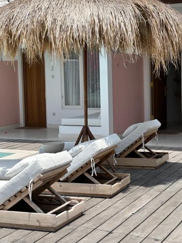 two lounge chairs and a straw umbrella on a deck at Love Song Boutique Hotel in Canggu