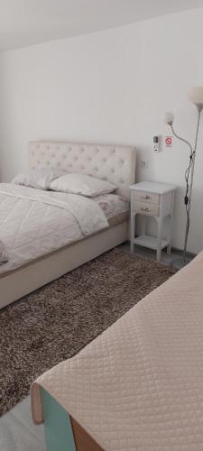 a white bedroom with a bed and a night stand at Fontana Apartman in Kruševac