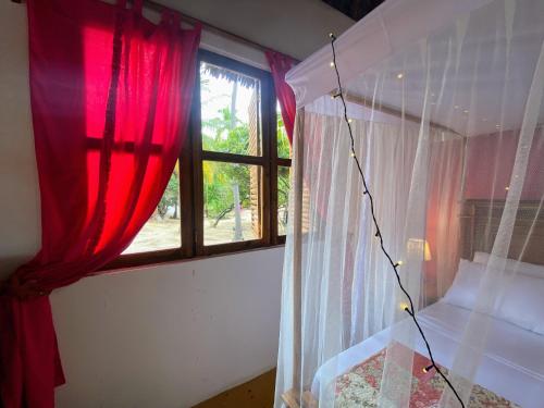 a bedroom with red curtains and a window at Jumapili Beach Villa in Ushongo Mabaoni