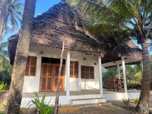 mały biały dom z dachem krytym strzechą w obiekcie Jumapili Beach Villa w mieście Ushongo Mabaoni