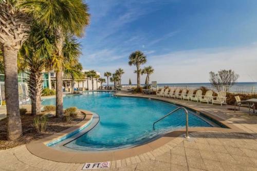 a swimming pool with palm trees and chairs next to the ocean at AQUA 1504 Beachfront condo with Free Beach Chairs in Panama City Beach