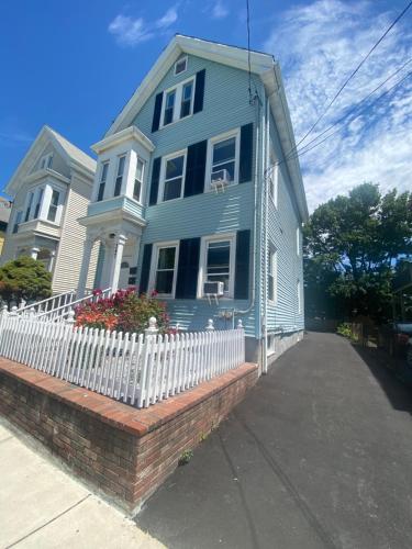une maison bleue avec une clôture blanche devant elle dans l'établissement Boston 2bd- Walk to Harvard, MIT, subway Parking, à Somerville