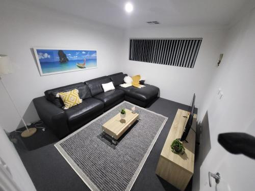 sala de estar con sofá negro y mesa en Comfort oasis family getaway, en Henley Brook