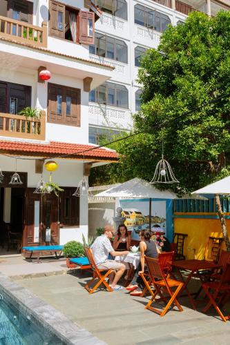a group of people sitting around a table by a pool at B'Lan Riverside Villa in Hoi An