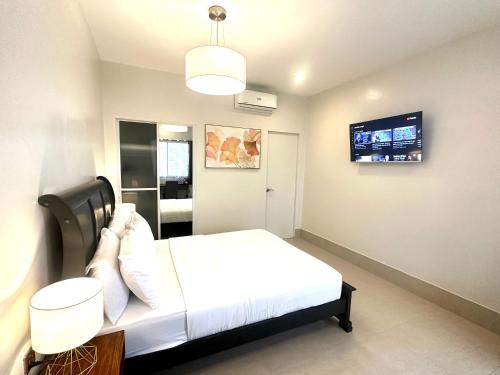 a bedroom with a white bed and a flat screen tv at HARMAN SUITES Moalboal in Moalboal