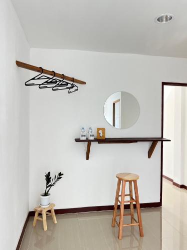 a white wall with a mirror and two stools at ปันสุขโฮมเทล Pansuk Hometel in Nakhon Phanom