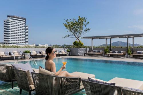 a woman sitting next to a swimming pool with a drink at Courtyard by Marriott Phuket Town in Phuket