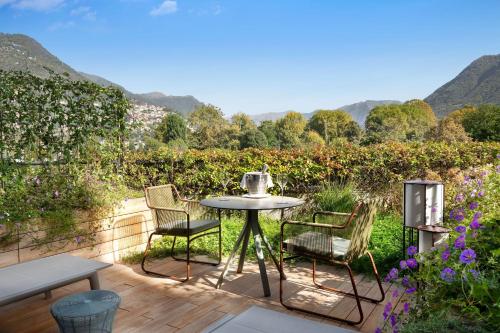 una mesa y sillas en una terraza de madera con montañas al fondo en Sheraton Lake Como Hotel, en Como