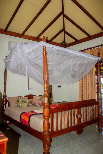 a canopy bed with a wooden frame with a white mosquito net at Mahi Villa in Bentota